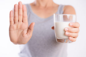 Woman hand holding glass of milk having bad stomach ache because of Lactose intolerance and another hand shows stop sign