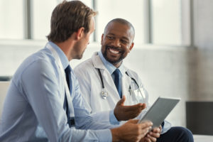 Two mature smiling doctors having discussion about patient diagnosis, holding digital tablet for Colorectal Cancer Screening