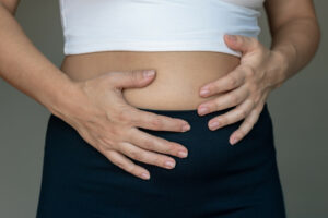A woman holding her stomach with her hands due to stomachache, bloating, heaviness, and digestive disorders.